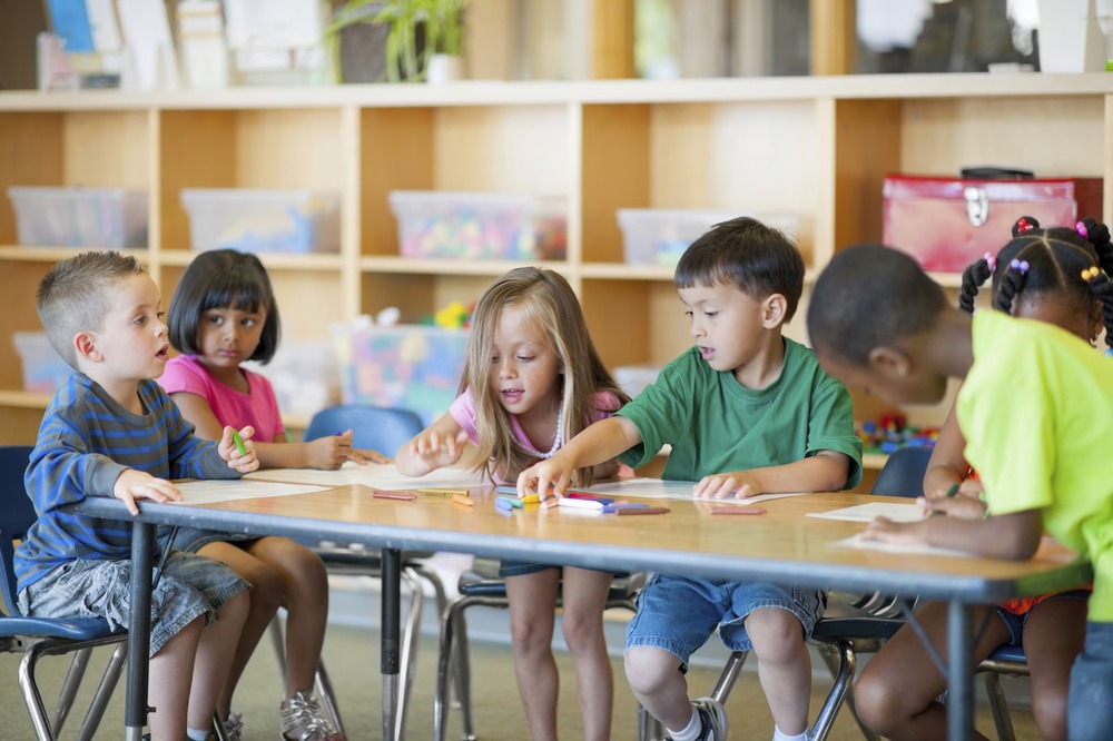Diverse group of young children engaged in drawing at a classroom table.