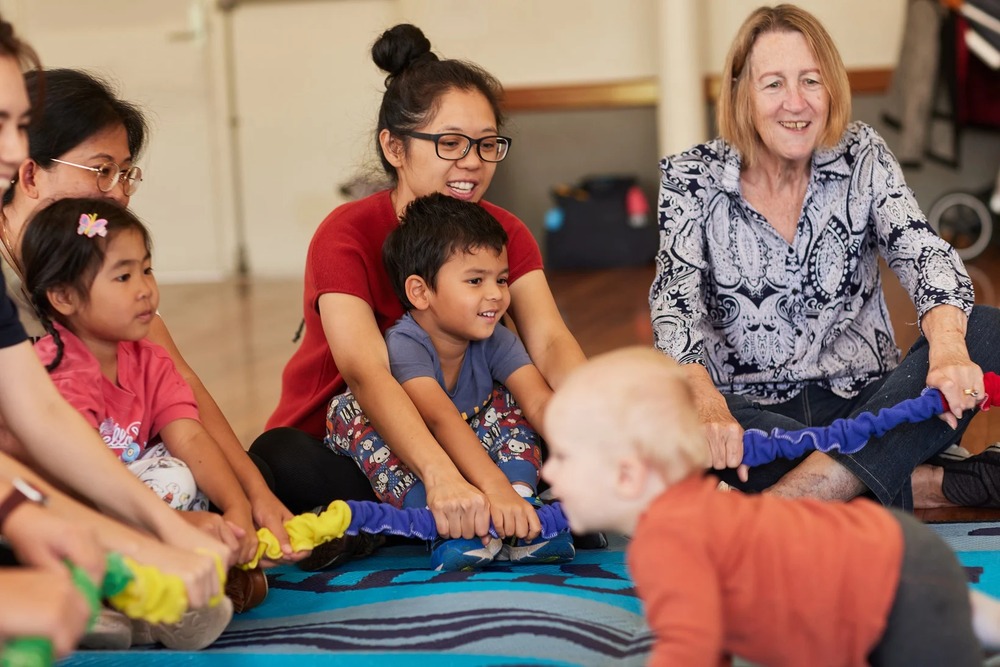 Children and adults playing with colorful ropes on a play mat.