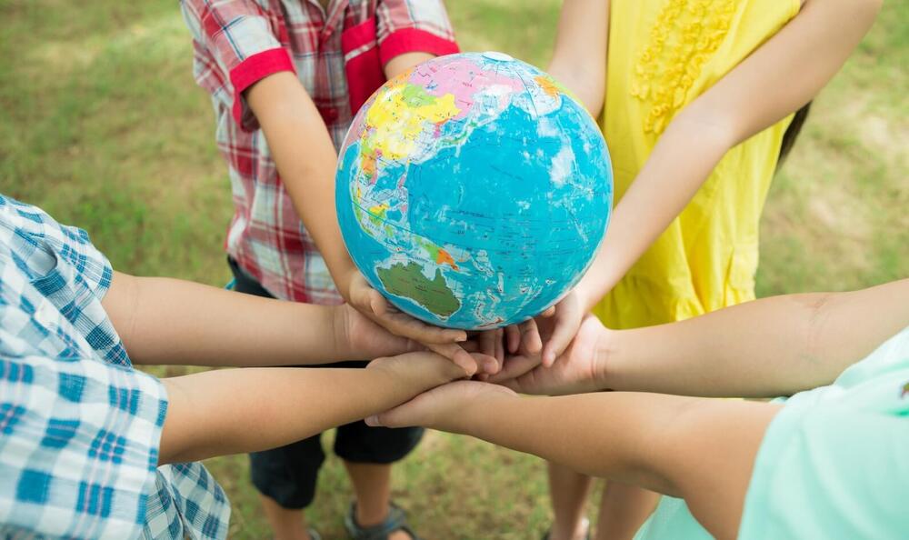 Children in colorful clothes holding a globe, symbolizing cultural awareness and diversity in education.