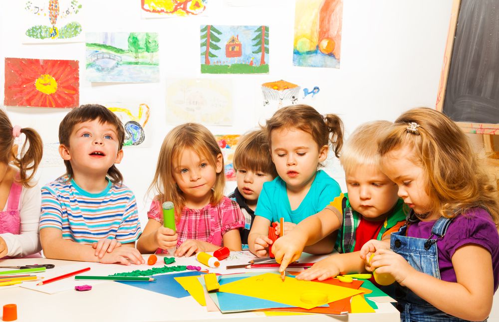 Children engaged in colorful art activities at a table, surrounded by vibrant drawings in a classroom setting.